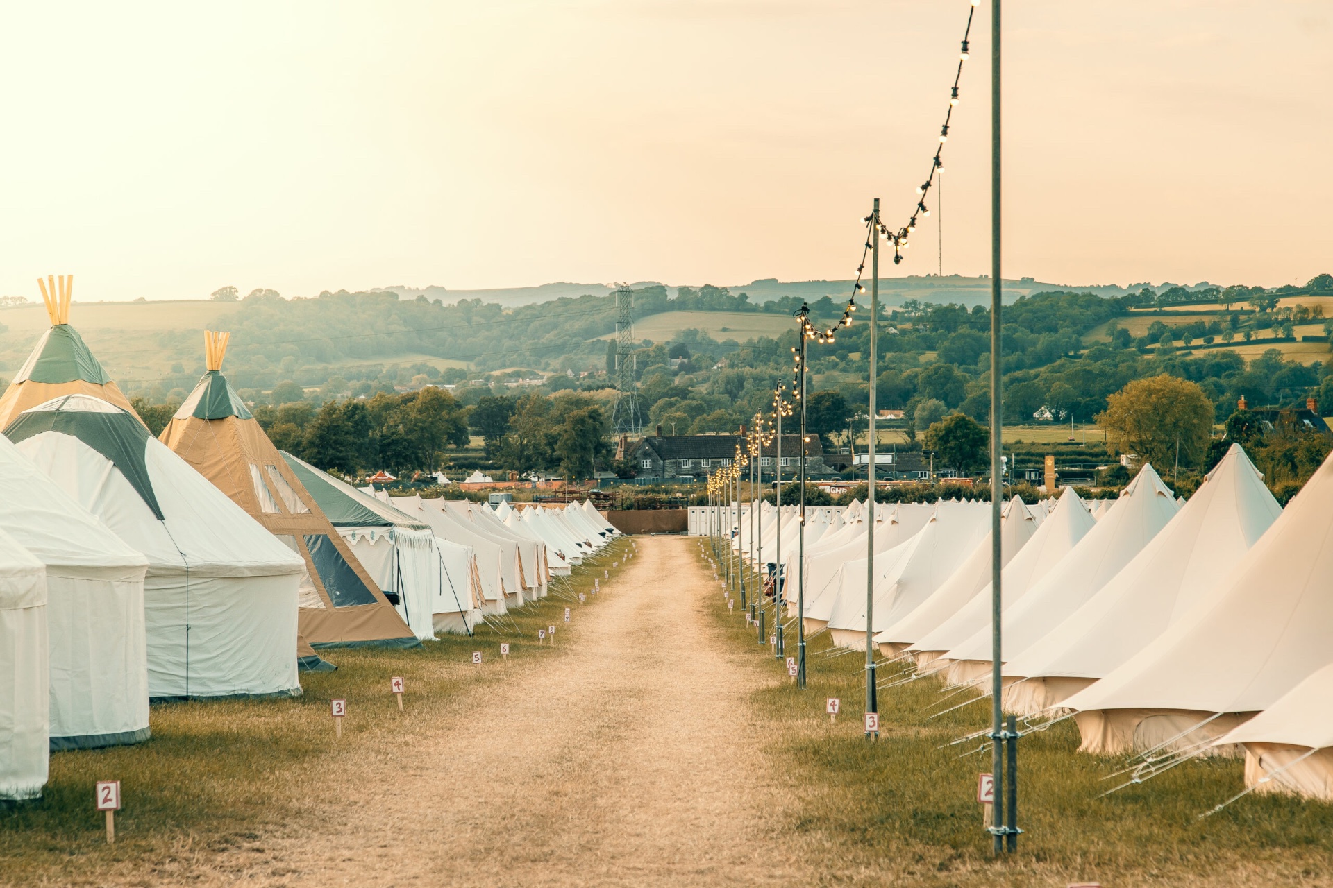 Rows of bell tents and tipis at golden hour beside a festoon-lit path
